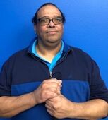 Photo of Michael Torres (Male, Hispanic) wearing blue and black striped shirt standing infront of solid blue wall.